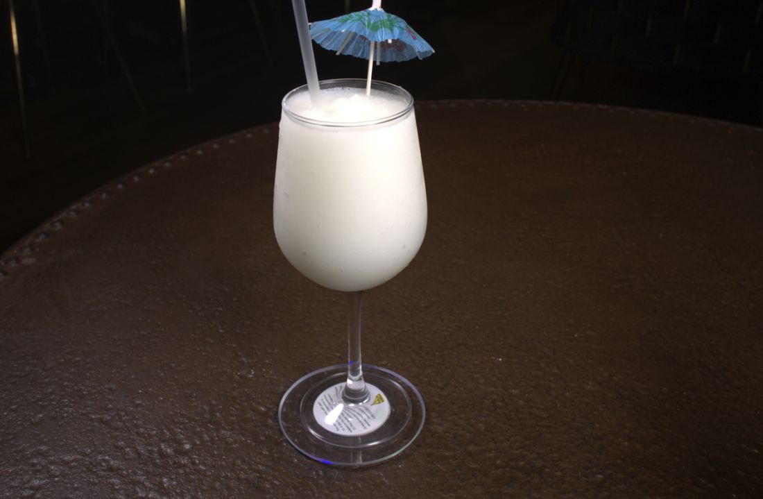 Creamy white drink in a wine glass with a cocktail umbrella